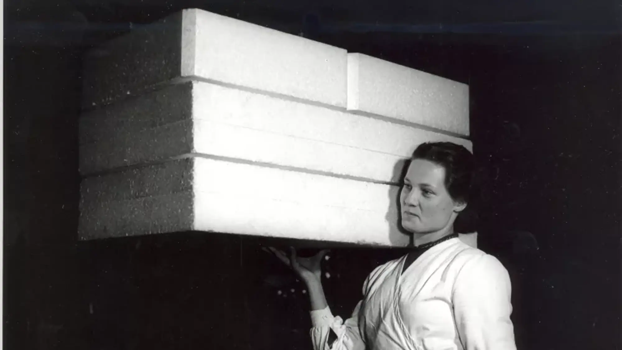 žena v bílém plášti nese tři bloky ze světlého, rozměrného, ale lehkého materiálu
