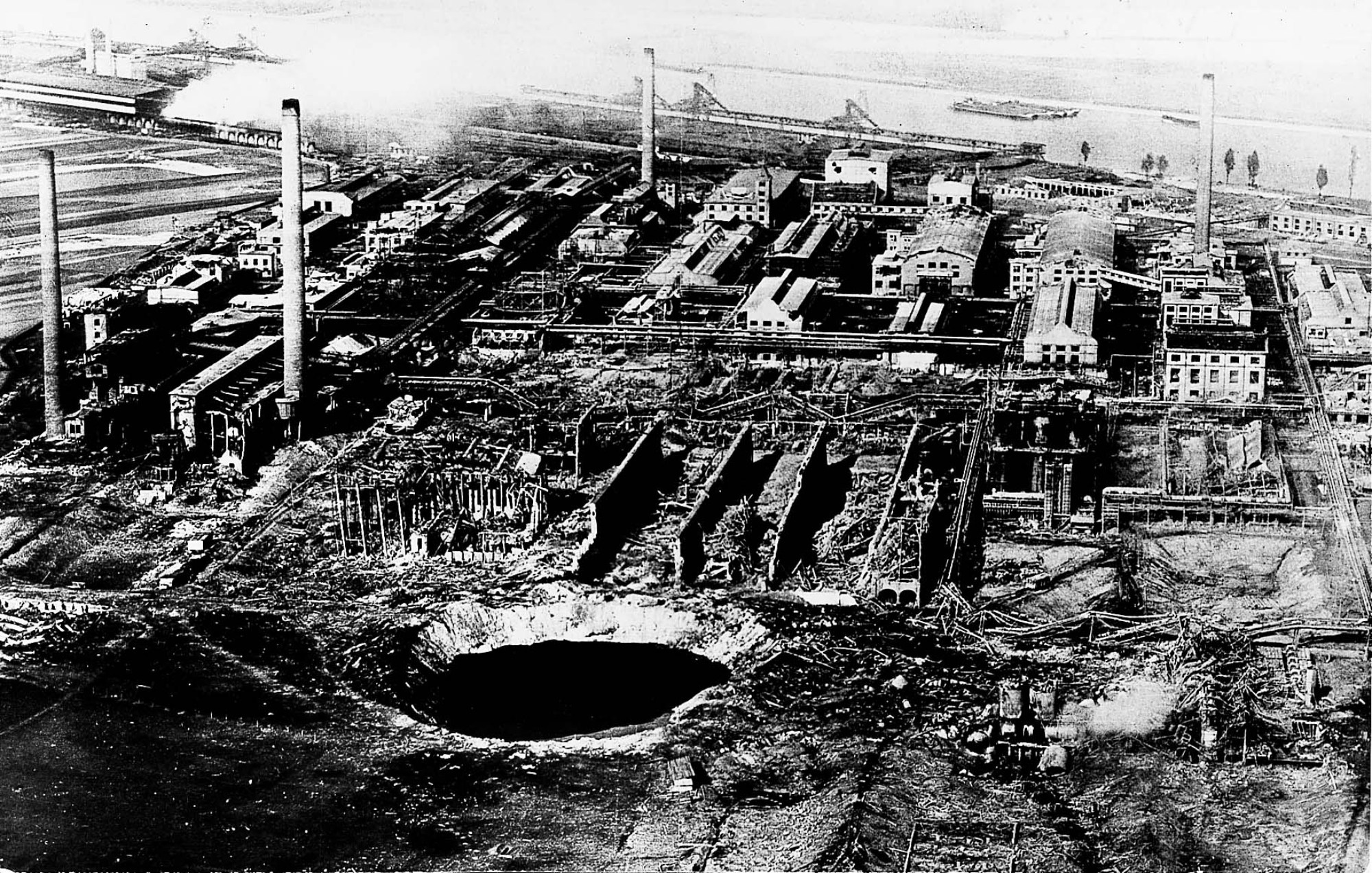 černobílý snímek ukazuje letecký pohled na továrnu s obrovským kráterem v popředí